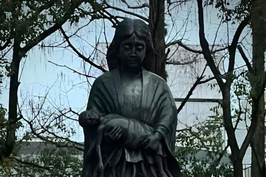 A statue of a person in a robe, surrounded by trees. 3