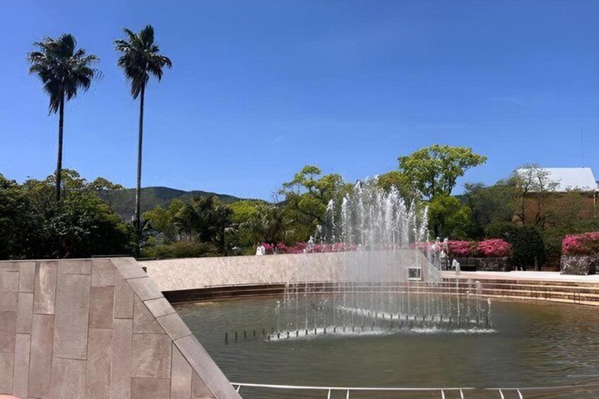 A fountain with water jets, surrounded by palm trees and flowering plants. 4