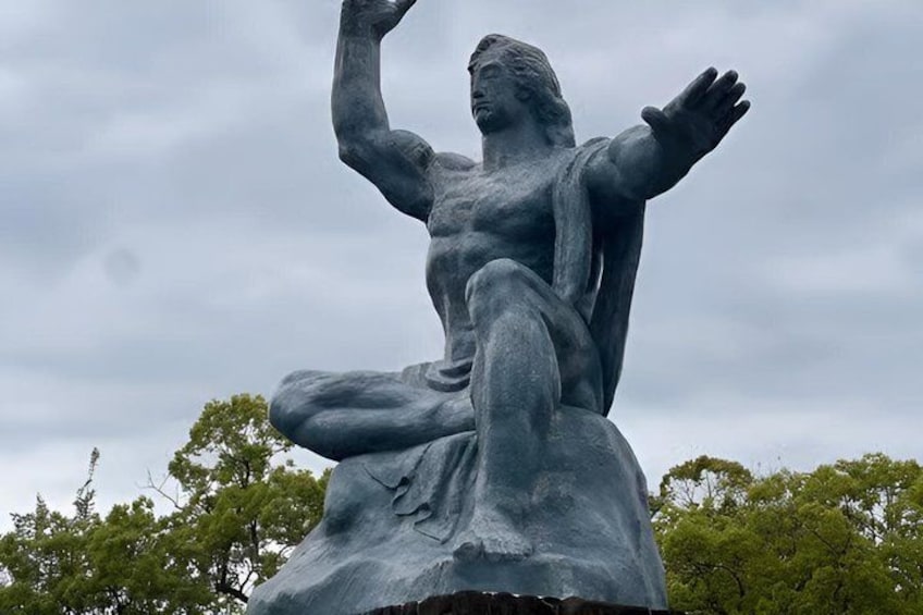 A large bronze statue of a seated man with outstretched arms, set against a cloudy sky. 1
