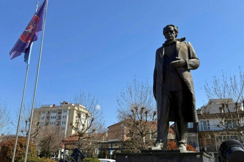 A statue of a man in a suit, a flagpole with a flag, and buildings in the background. 3