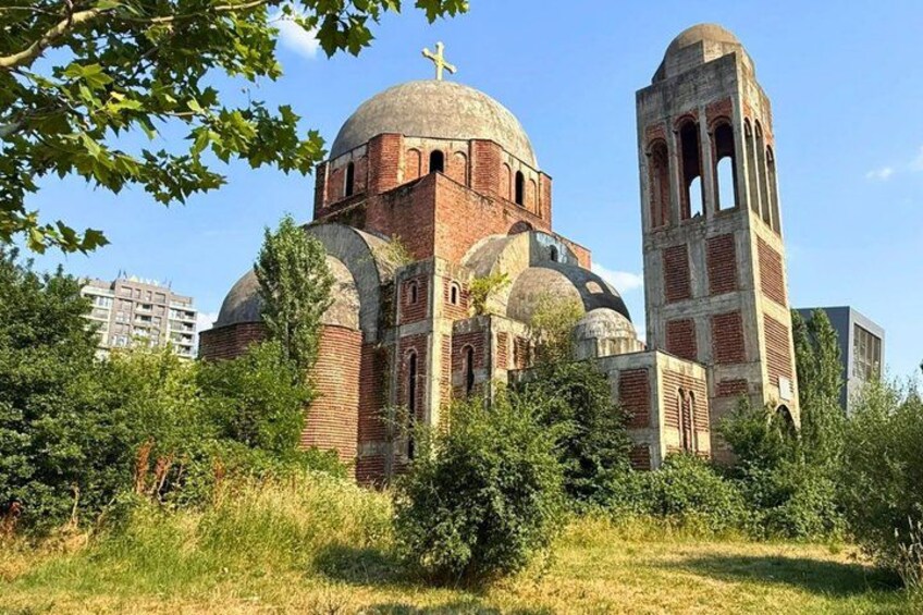 A historic church with domed architecture and bell towers, surrounded by greenery and urban buildings. 2