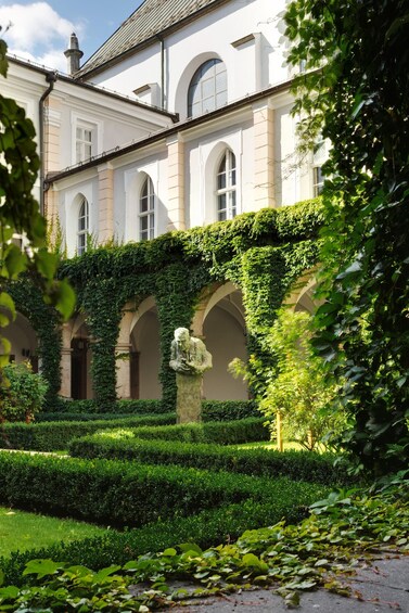 Un edificio clásico con ventanas arqueadas y un patio con setos cuidados y una estatua. 2