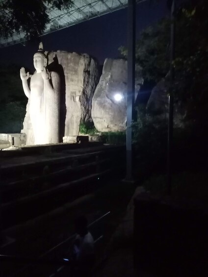Une grande statue représentant une figure en position élevée, se détachant sur un arrière-plan composé de formations rocheuses imposantes et d’un ciel nocturne. 3