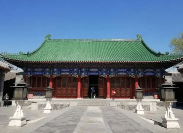 A traditional Chinese building with a green roof, red pillars, and statues in front. 2