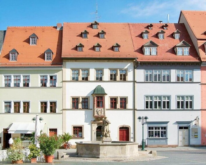 Une place de ville européenne, avec des bâtiments traditionnels, une fontaine centrale et un ciel d’un bleu éclatant. 2