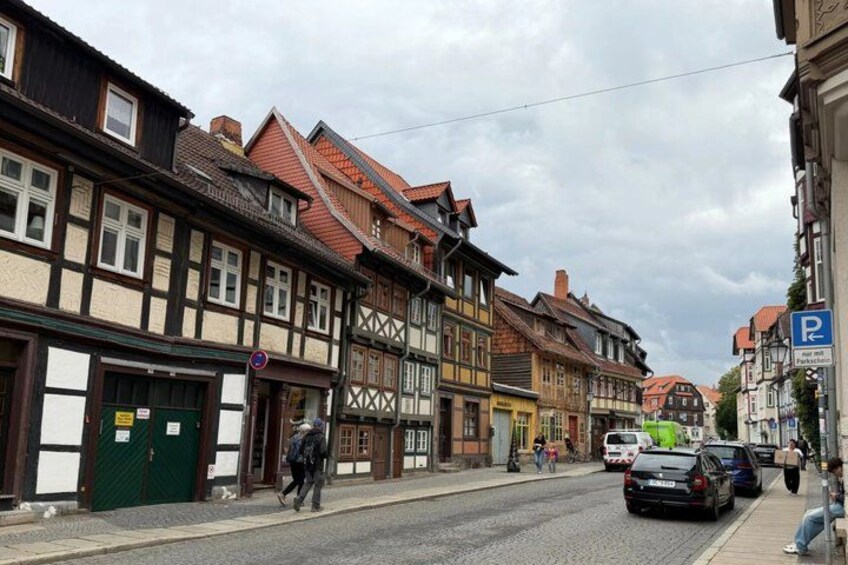 A cobblestone street lined with traditional half-timbered houses, a pedestrian, and parked cars. 4