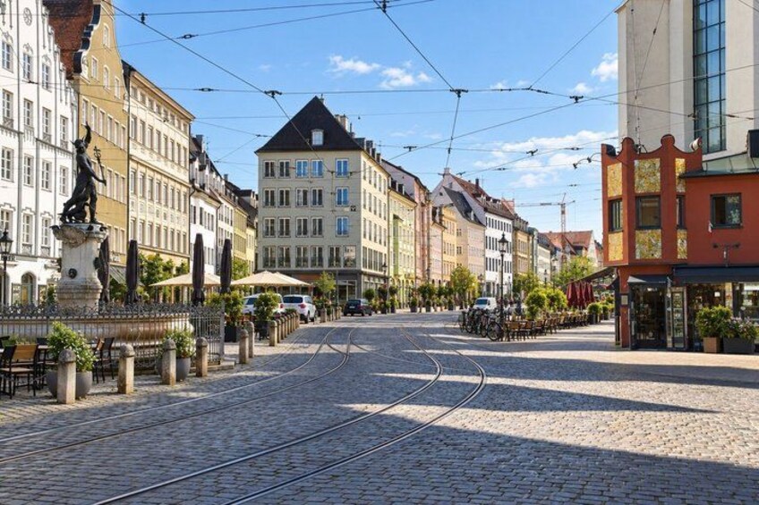 A cobblestone street with tram tracks, historic buildings, and a statue. 2