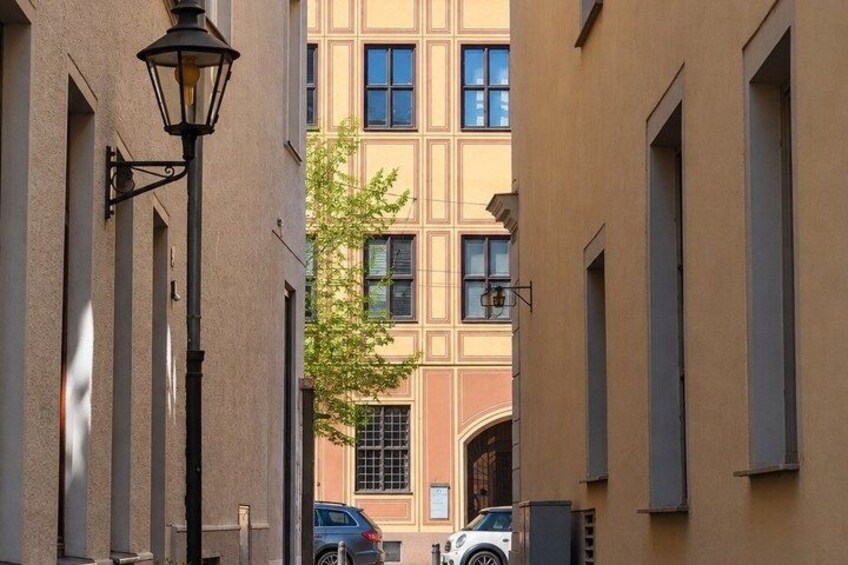 A narrow street with buildings, a street lamp, and parked cars. 3
