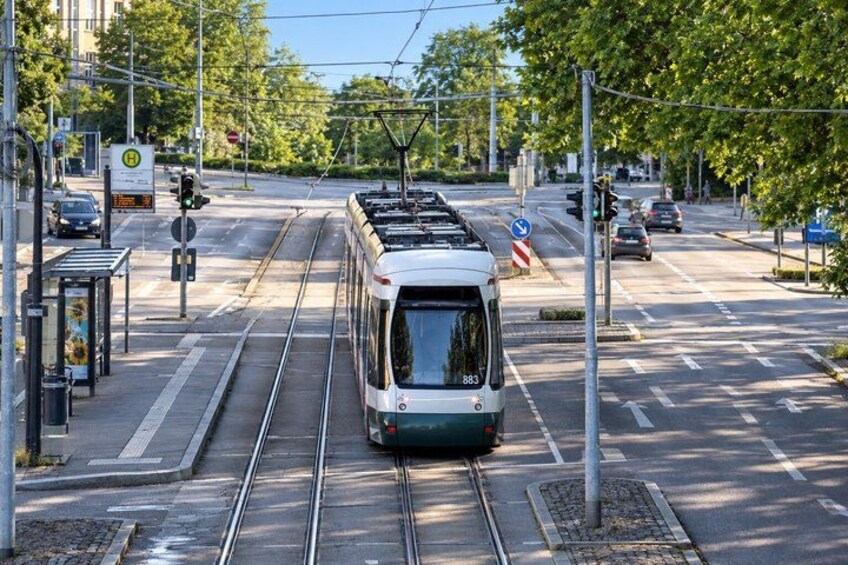 A tram on tracks at a city intersection with traffic lights and a bus stop. 5