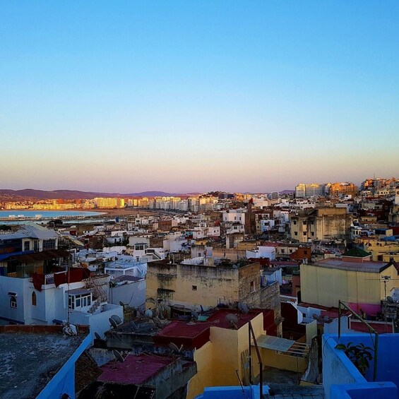 A densely packed urban area with a mix of residential and commercial buildings, a clear sky, and a distant view of a coastline. 1