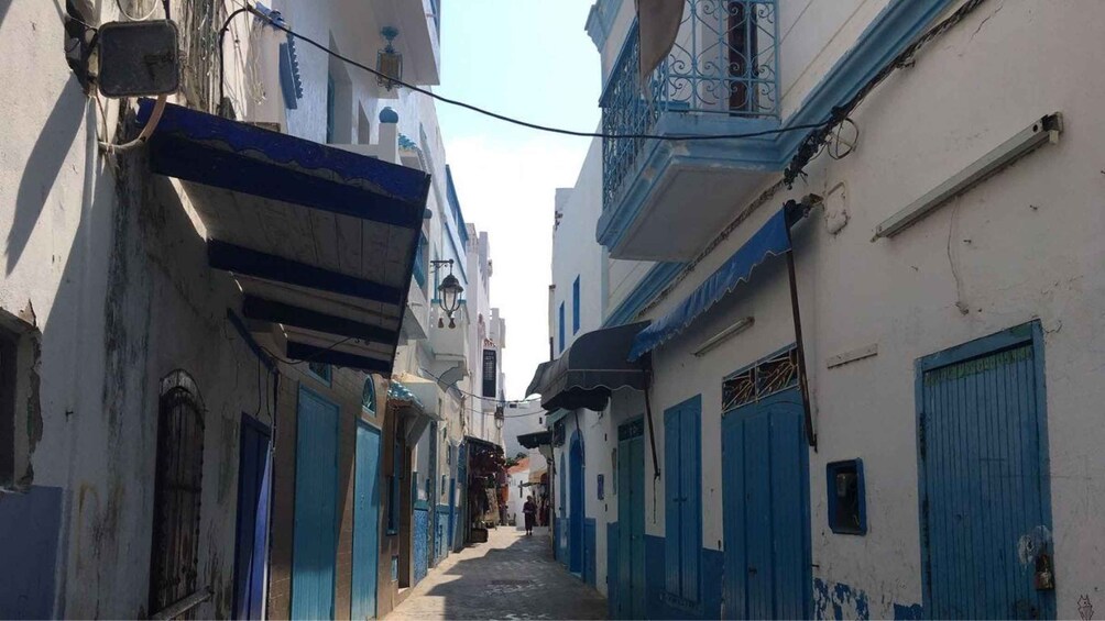 A narrow street with buildings painted in blue and white, featuring balconies and doors. 5