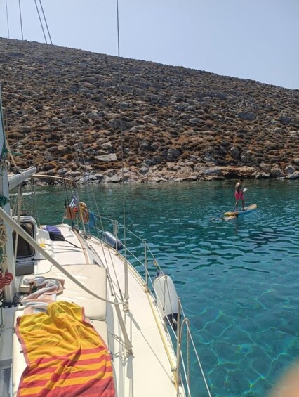 A boat with a person paddleboarding in clear water near a rocky shoreline. 2