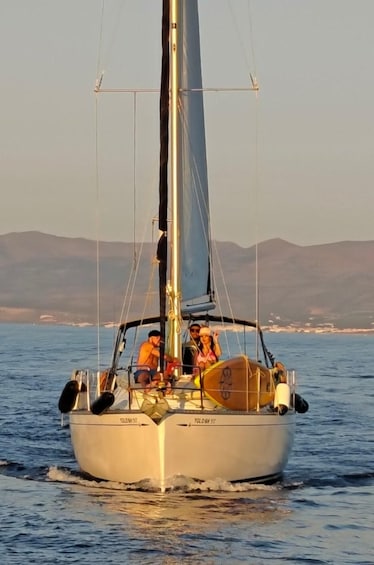 A sailboat with people on board, sailing on calm waters with a mountainous coastline in the background. 5