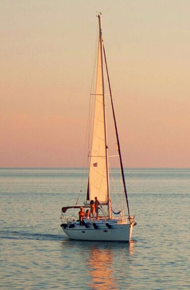 A sailboat with a single mast and a small cabin, sailing on calm waters during sunset. 1