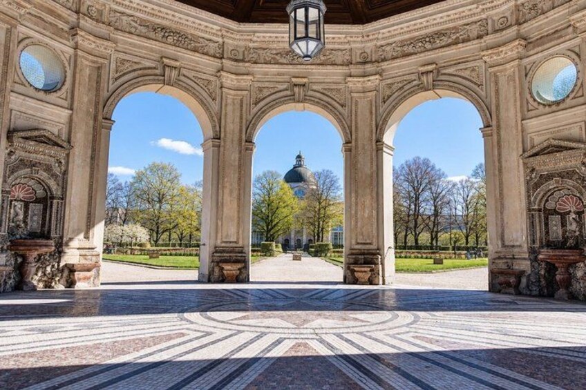A historical building with ornate columns and a patterned floor, leading to a distant dome structure. 3