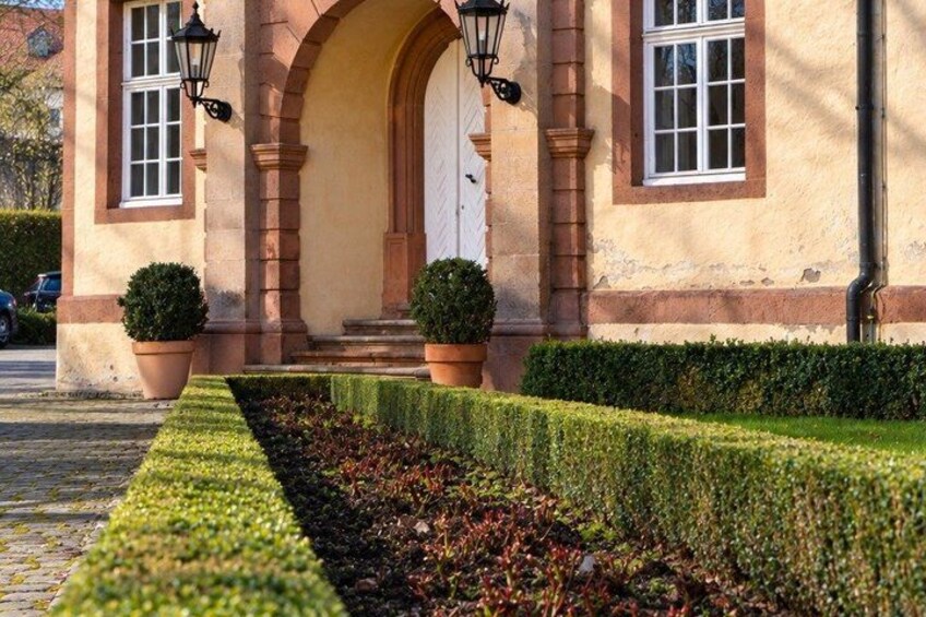 A building with a white door, two potted plants, and a neatly trimmed hedge. 2