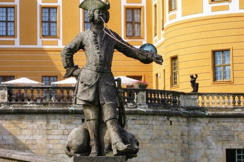 A statue of a historical figure with a sword and a globe, set against a yellow building with windows. 4