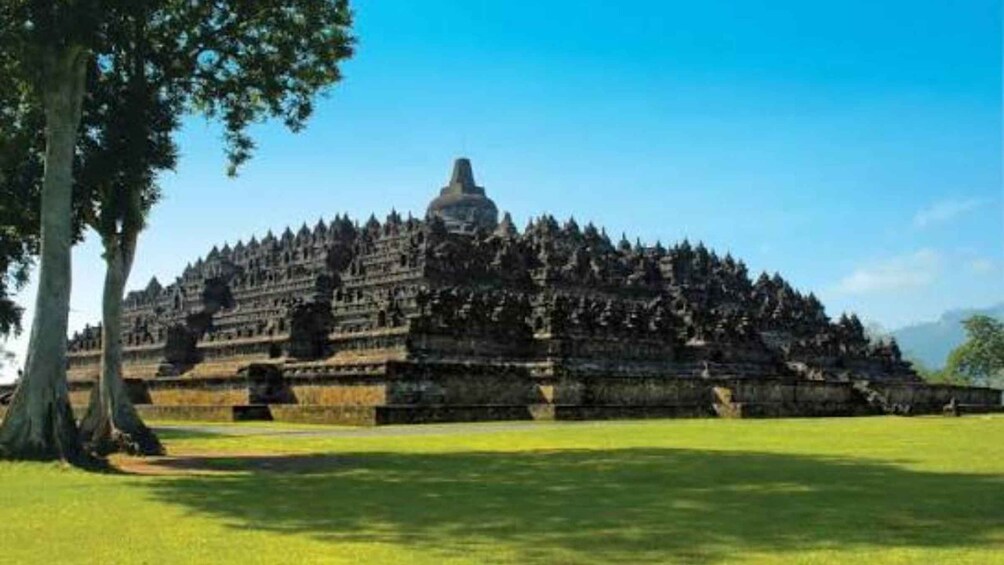 A large, tiered temple complex with a prominent central stupa, surrounded by lush greenery and trees. 3