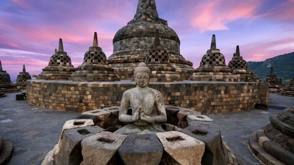 A stone Buddha statue in a meditative pose, surrounded by a circular stone platform, with a temple complex in the background. 2