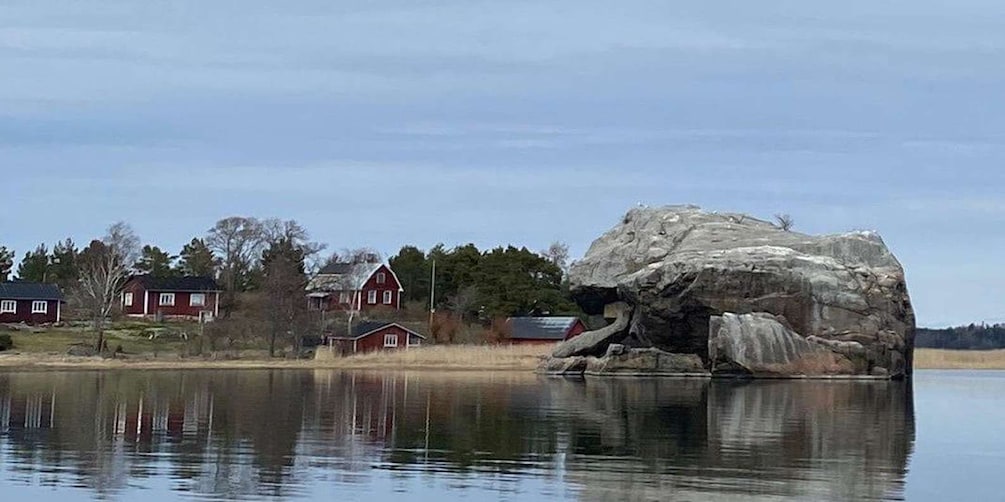 A large rock formation near a body of water with houses in the background. 5