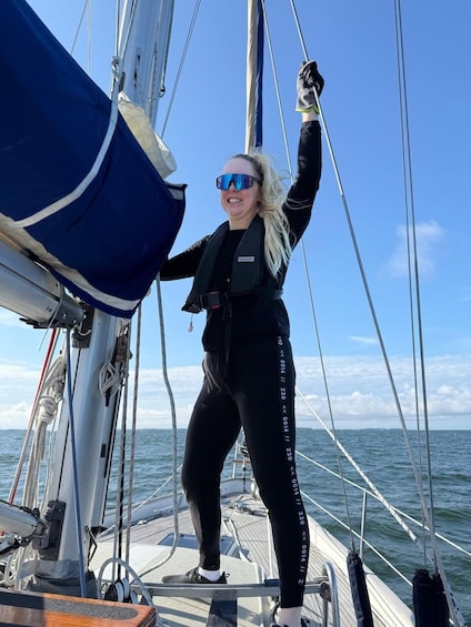 A person on a sailboat, wearing a life jacket and holding onto a sail. 4