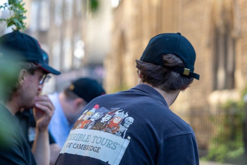 A person wearing a dark t-shirt with a graphic and text on the back, standing outdoors. 1
