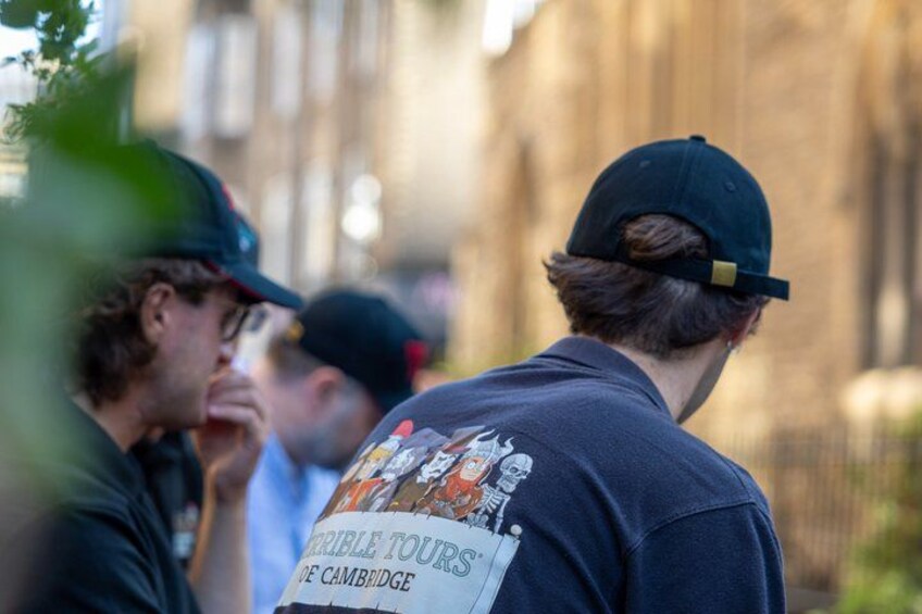 A person wearing a cap and a t-shirt with a graphic design, standing outdoors with a blurred background. 5