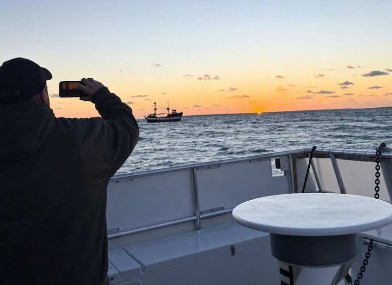 A person taking a photo of a sunset with a ship in the background. 4