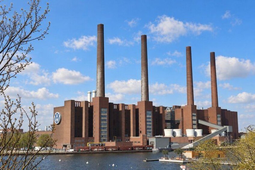 A large industrial facility with multiple tall chimneys, a river in the foreground, and a clear blue sky. 5