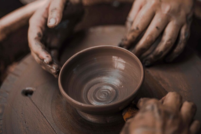 Hands shaping a clay pot on a spinning wheel. 1
