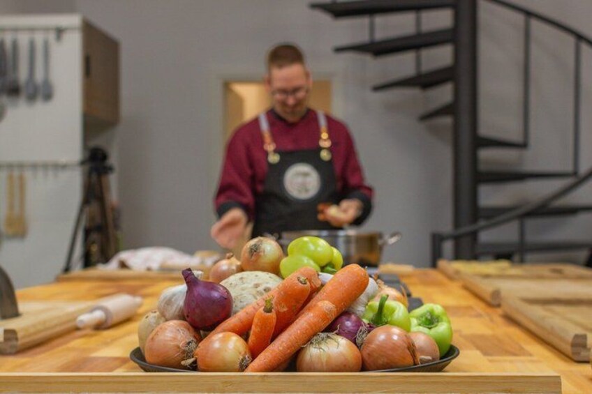 A kitchen with a variety of vegetables on a cutting board and a person in the background. 2