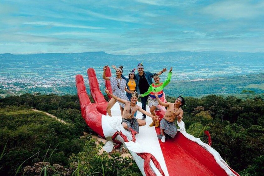 A group of people sliding down a large red slide with a scenic view of a city and mountains in the background. 5