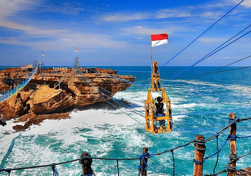 A rocky coastal area with a flag-raising ceremony, ropes, and a person on a platform. 1