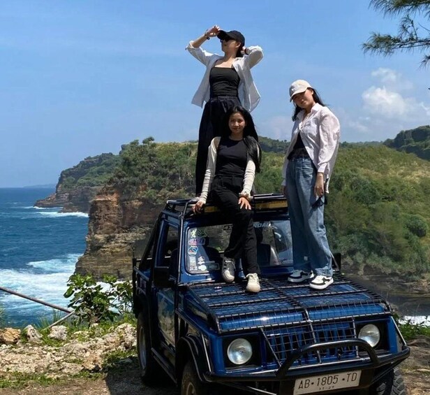 A blue off-road vehicle parked on a cliff with two people standing on top. 2