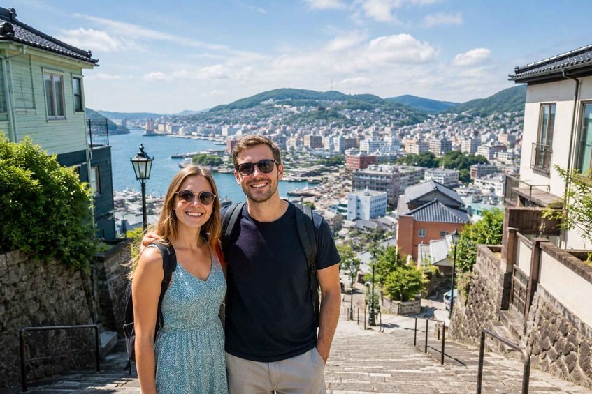 A couple standing on a stone staircase overlooking a city with a body of water and hills in the background. 1