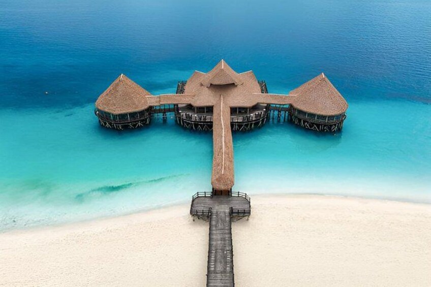 An overwater bungalow with a thatched roof and a wooden walkway leading to it. 2