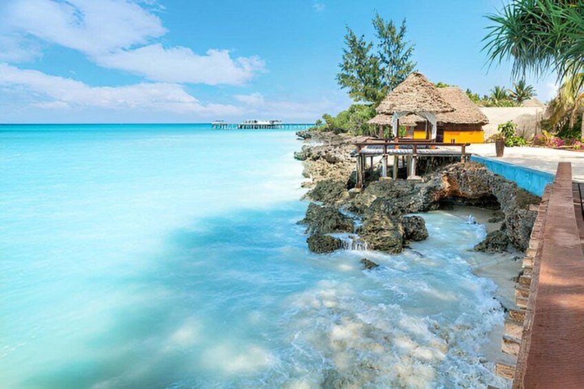 A tropical beach with clear turquoise water, a thatched-roof hut, and a wooden pier extending into the ocean. 4