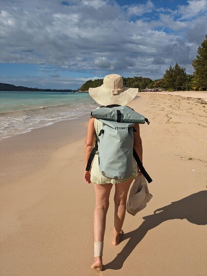 Une personne se promène sur une plage de sable, portant un grand chapeau et un sac à dos bleu clair. 1