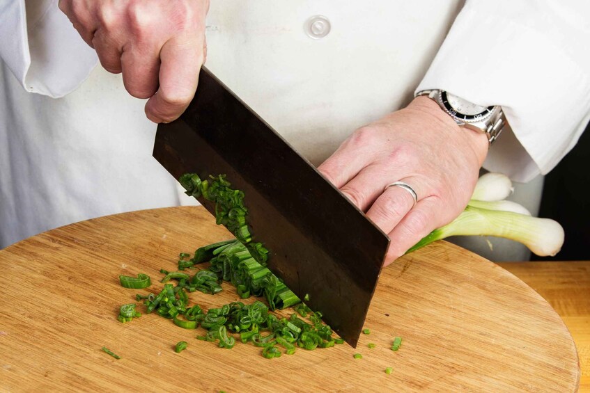A person chopping green onions on a wooden cutting board. 2