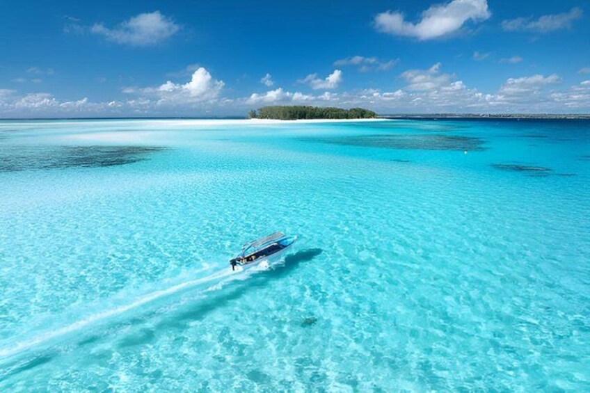 A clear blue sea with a boat creating a wake, surrounded by a tropical island and a clear sky. 2