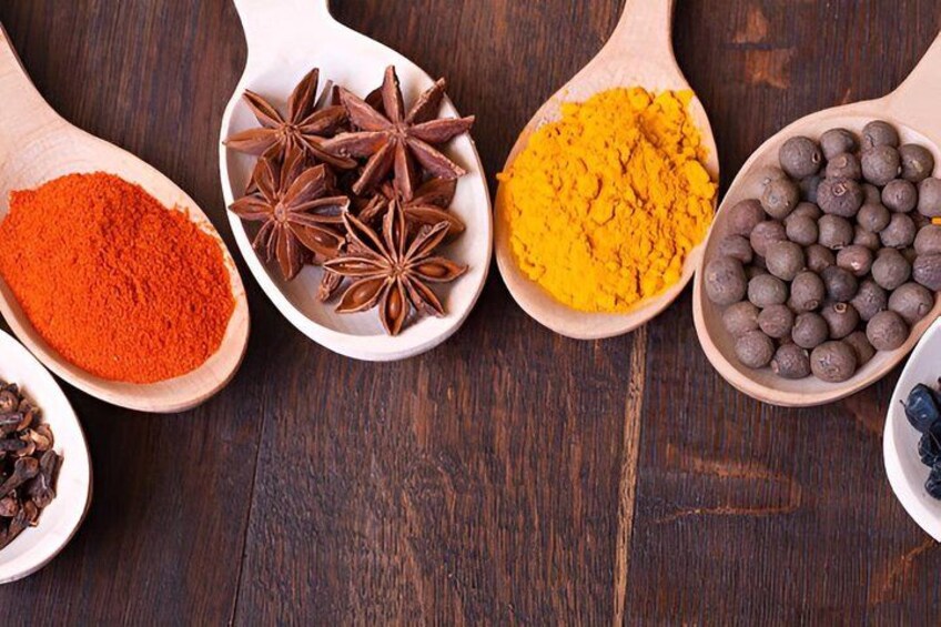 Four wooden spoons containing different spices on a wooden surface. 4