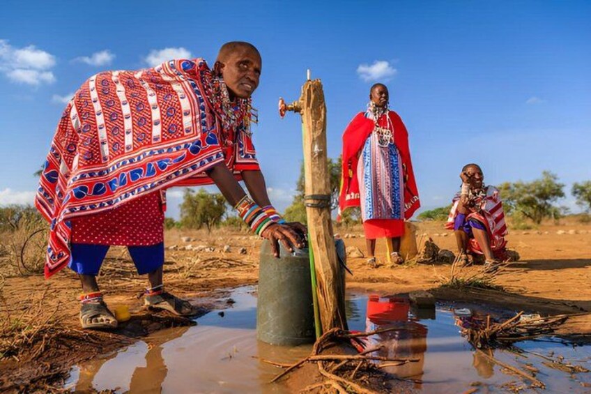 People in traditional attire near a water source in a dry landscape. 4