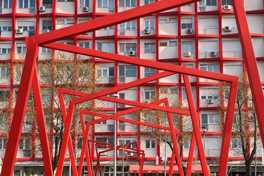 A red metal structure in front of a building with multiple windows and air conditioning units. 2