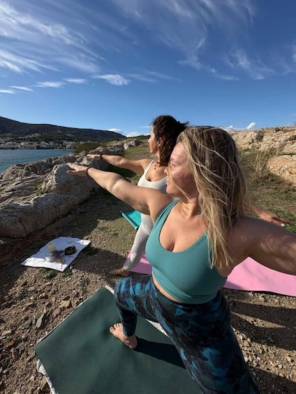 Deux personnes pratiquent le yoga sur des tapis, au bord de la mer, sur un terrain rocheux, sous un ciel dégagé. 2