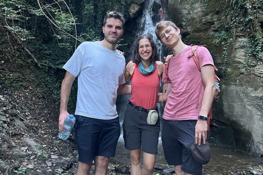 Three people standing in front of a waterfall with greenery in the background. 5