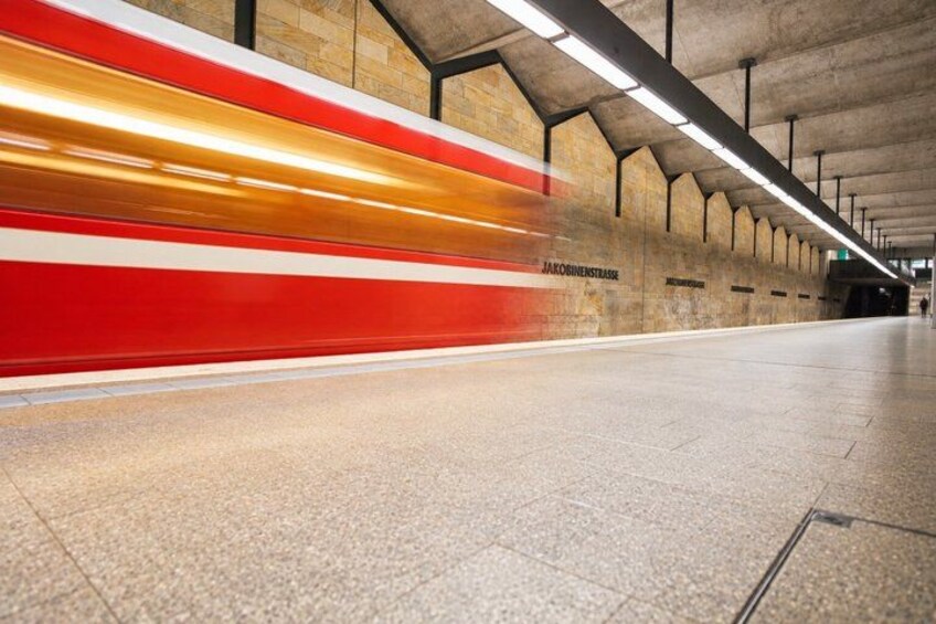 A subway train with red and white stripes passing through a station with stone walls and overhead lighting. 4
