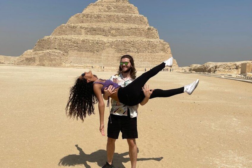 A person holding another person in a desert with a pyramid in the background. 1