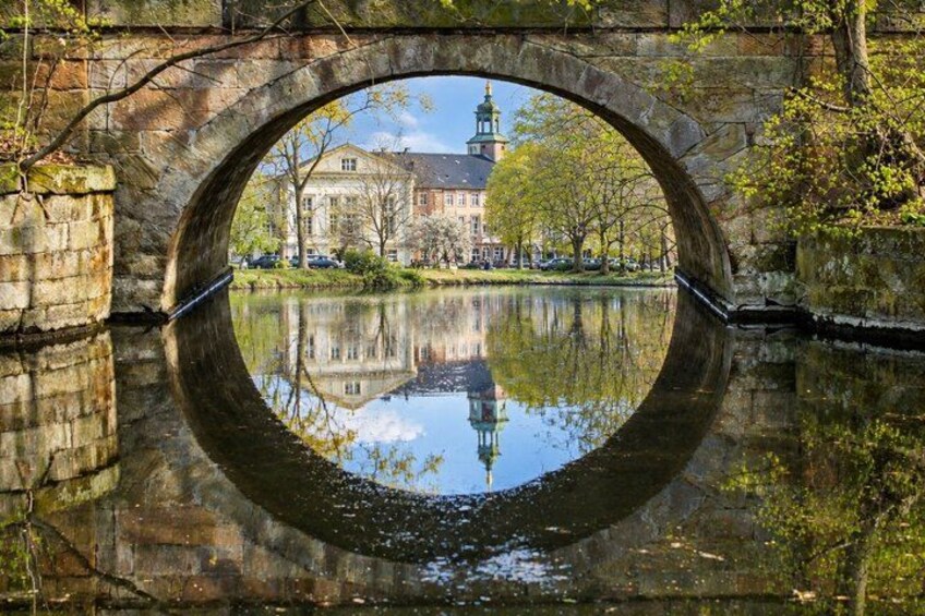 A stone bridge arching over a calm river, reflecting a building and trees. 2
