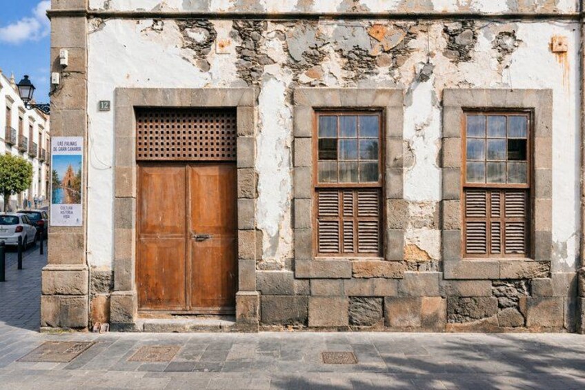 A weathered building with a large wooden door and two windows with shutters. 2