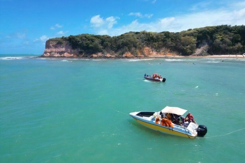 A boat on turquoise water with a cliff and beach in the background. 4